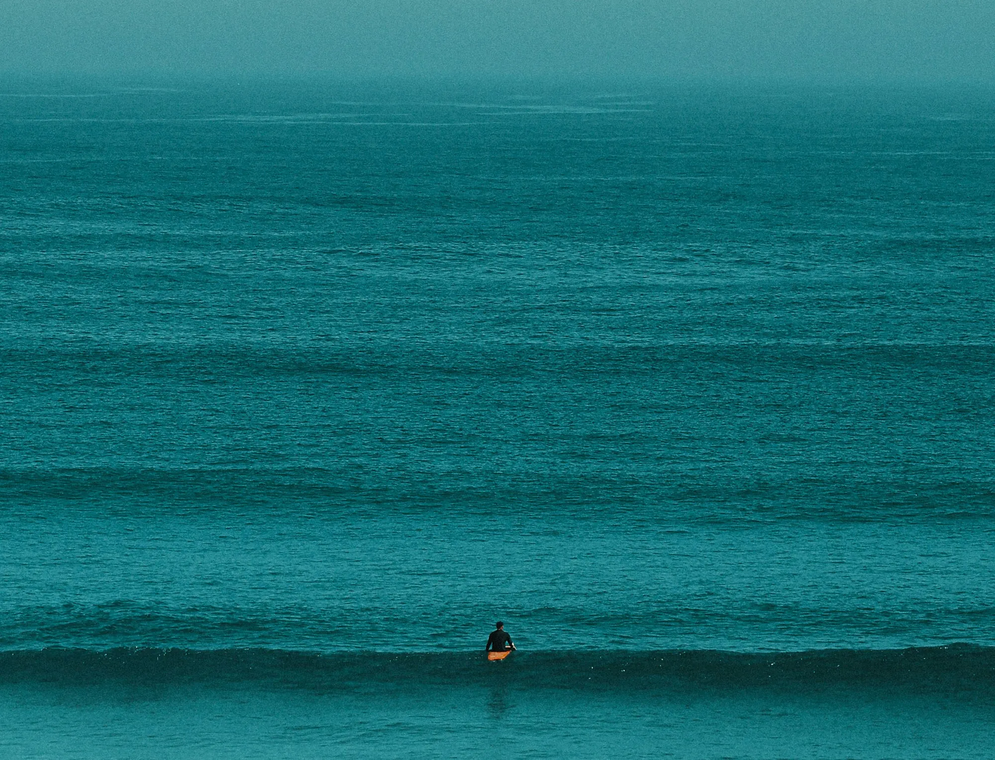 man sitting on surfboard over vast cyan ocean